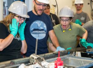 From left: Beth Novak (Assistant Laboratory Officer, IODP JRSO), Christophe Galerne (Physical Properties Specialist, GEOMAR Helmholtz Centre for Ocean Research Kiel, Germany), and Susan Boehm (Marine Laboratory Specialist, IODP JRSO) react excitedly to the sill obtained in a core. (Credit: Tim Fulton, IODP JRSO) [Photo ID: exp385_081]